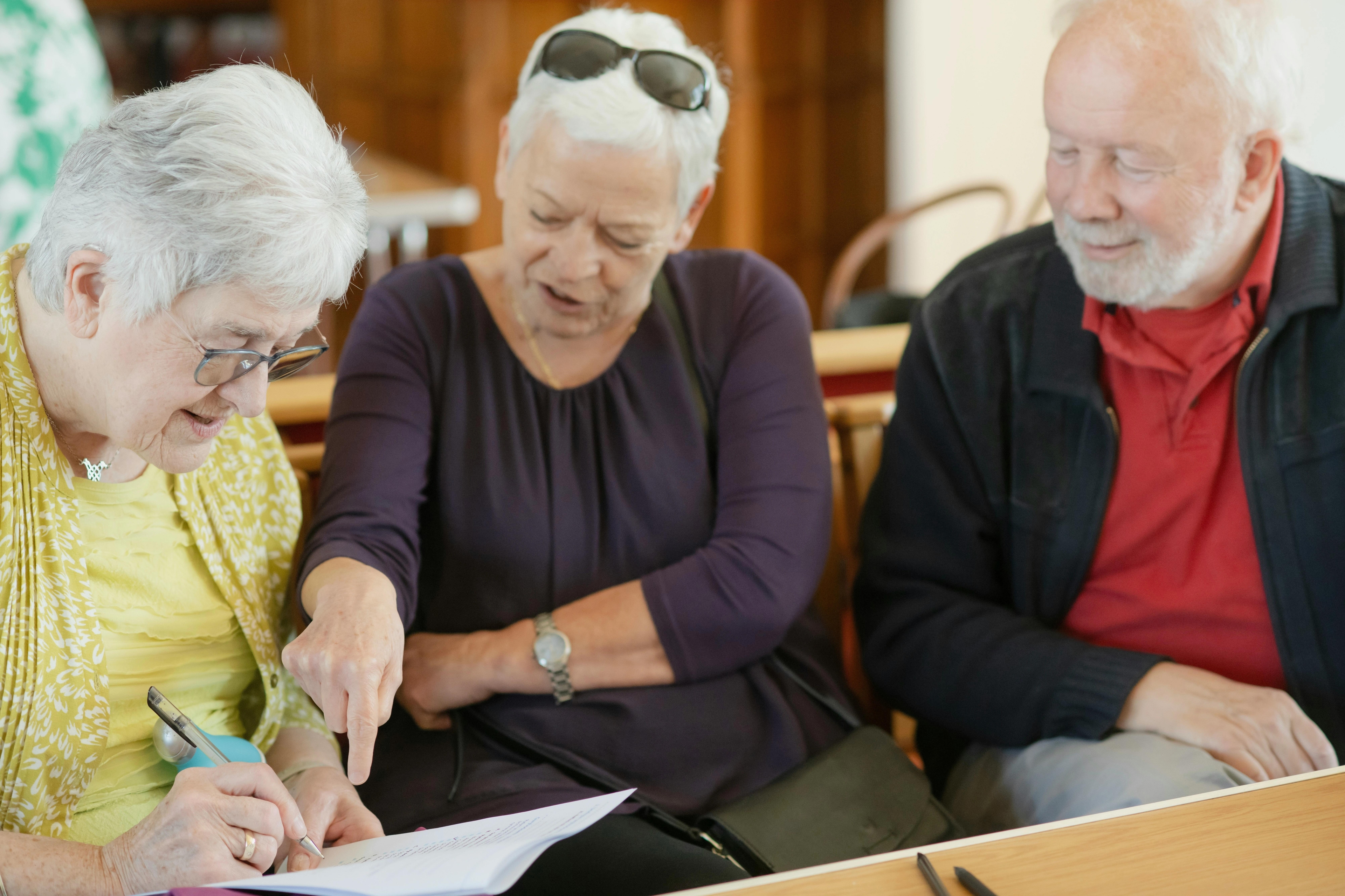 A woman sitting in the middle of an older woman and older man, helping them do paperwork.